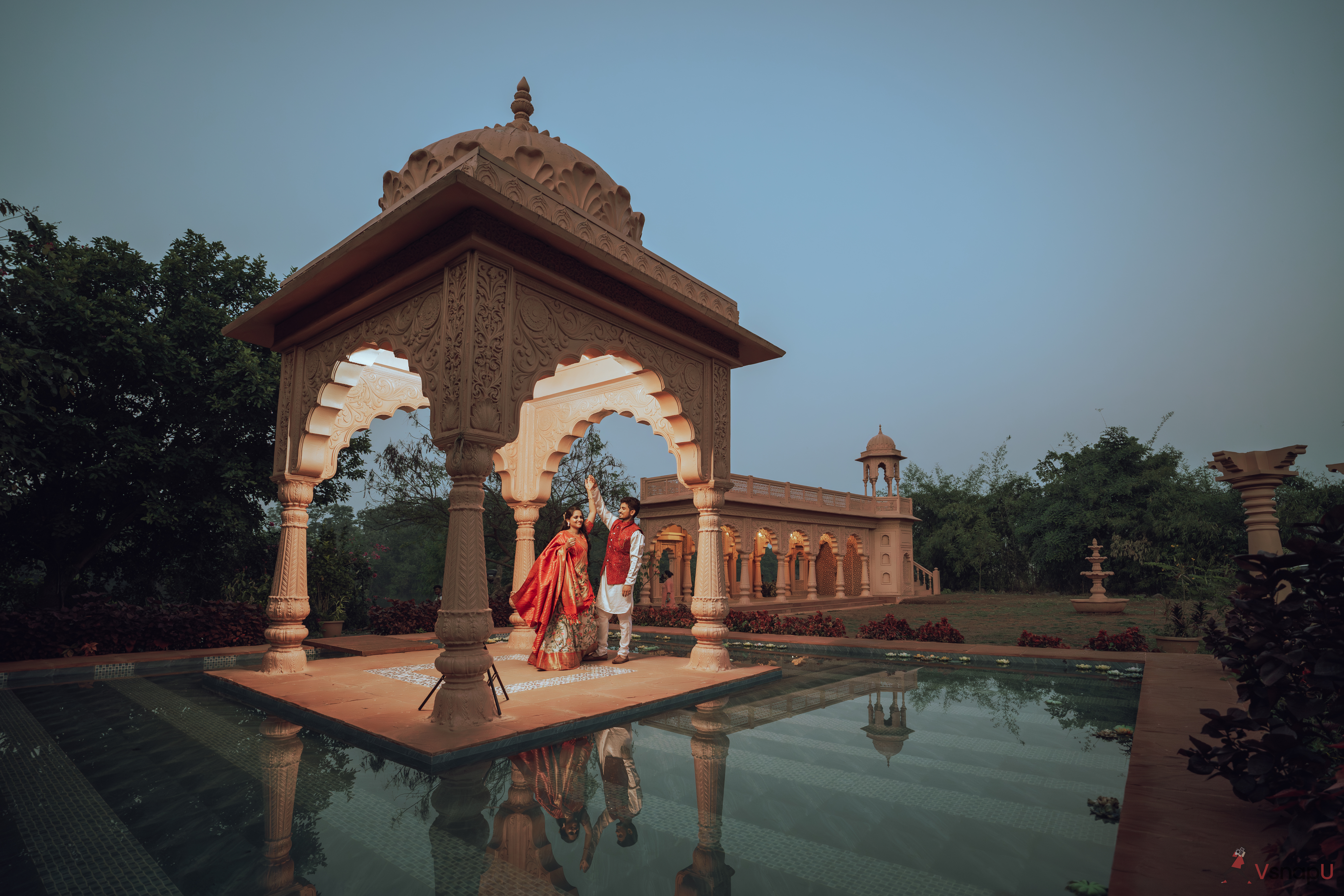 In the enchanting setting of a Rajasthani tomb, a couple in ethnic wear dances joyfully next to a tranquil pond.